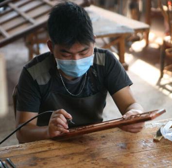 工厂内，工人在往木材上雕刻纹路 